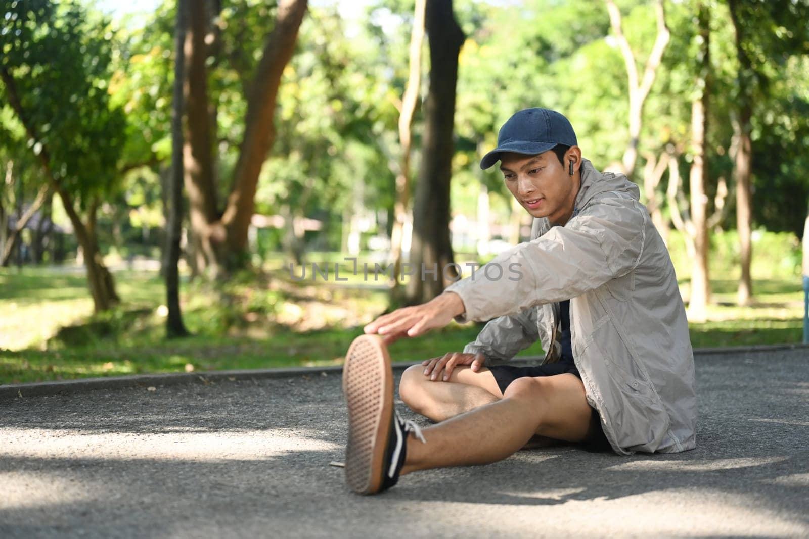 Young sporty man stretching outdoors before running in nature during sunny summer day.
