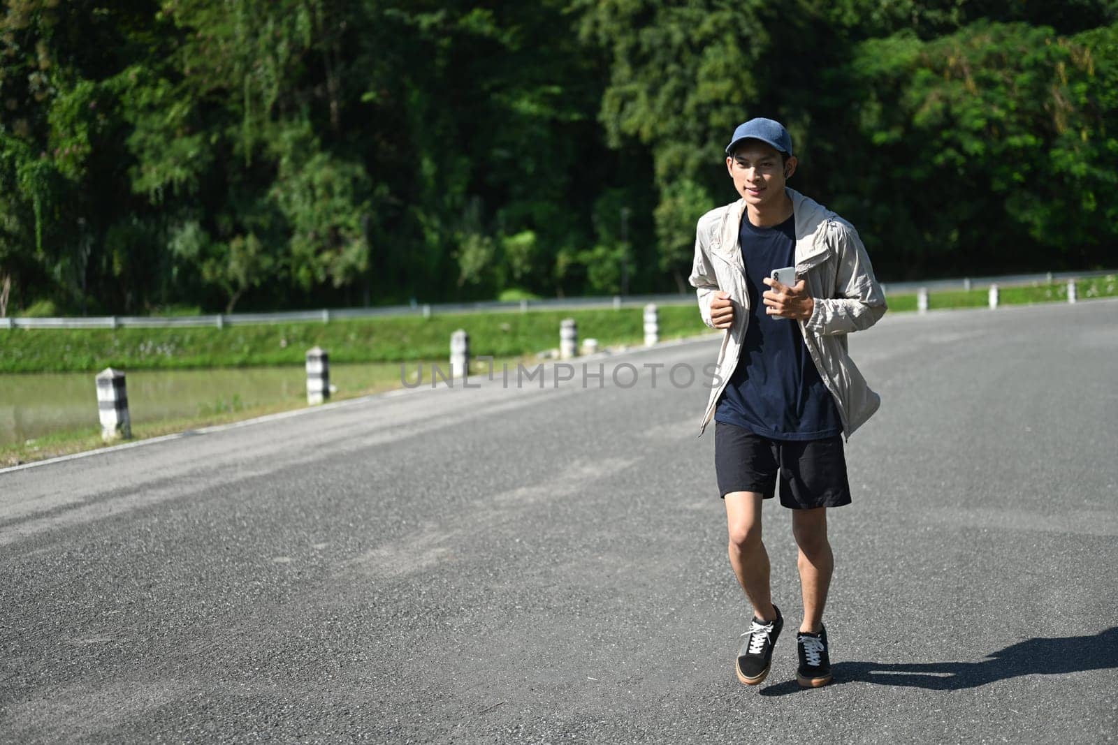 Active young asian man jogging by a riverside path on sunny day.
