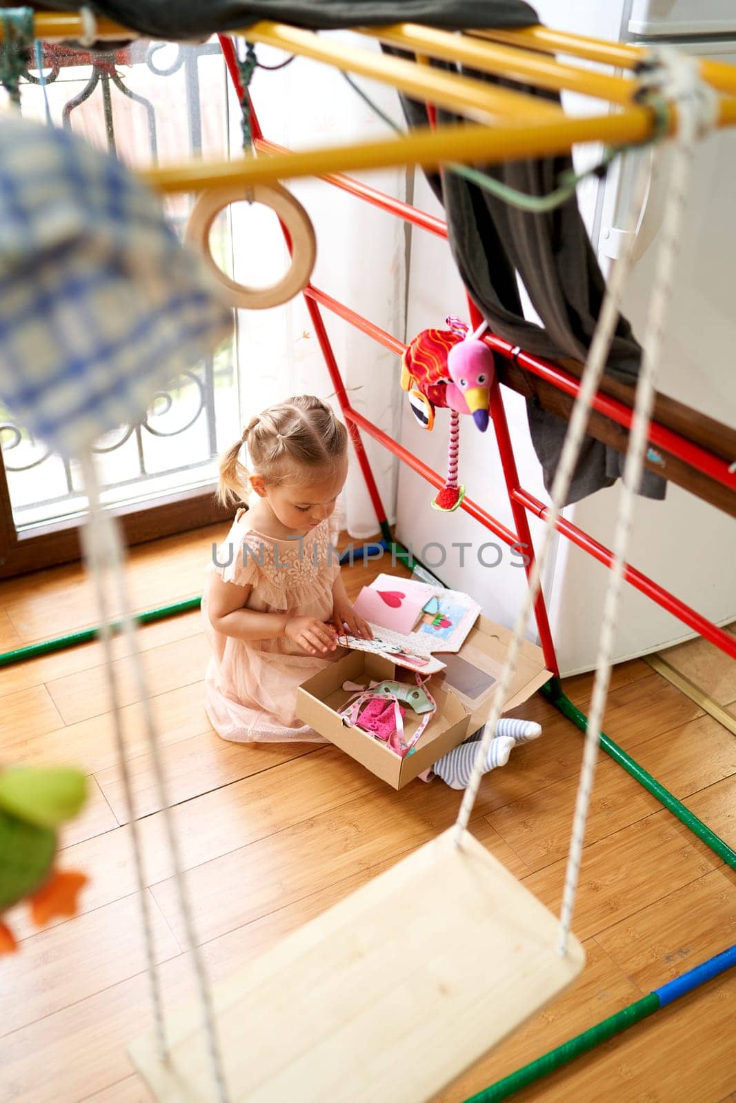 Little girl sits on the floor in a room near a swing and looks at postcards. High quality photo