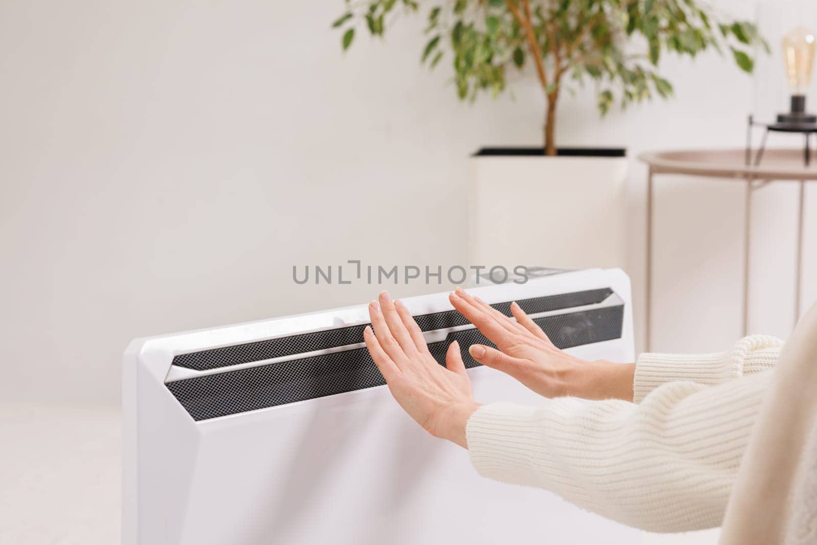 Unwell woman renter in blanket sit in cold living room hand on old radiator.suffer from lack of heat . Unhealthy young woman struggle from chill freeze at home. No heating concept.