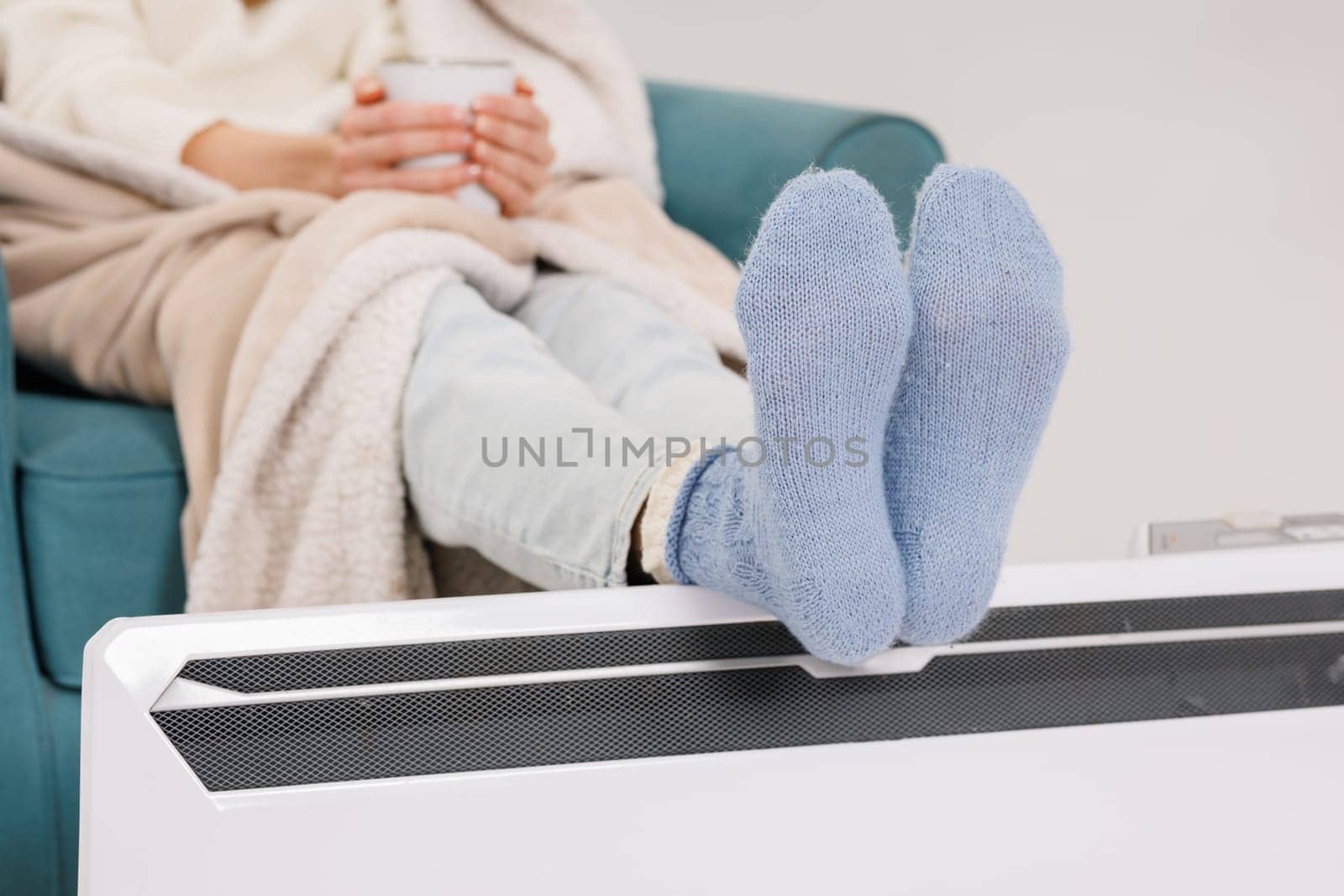 Young girl in warm knitted socks warms her feet on a radiator. Heating season concept.