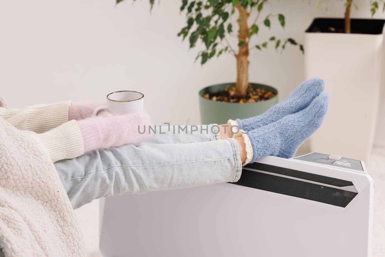 Young girl in warm clothes and with a cup of tea at home. Heating season concept.