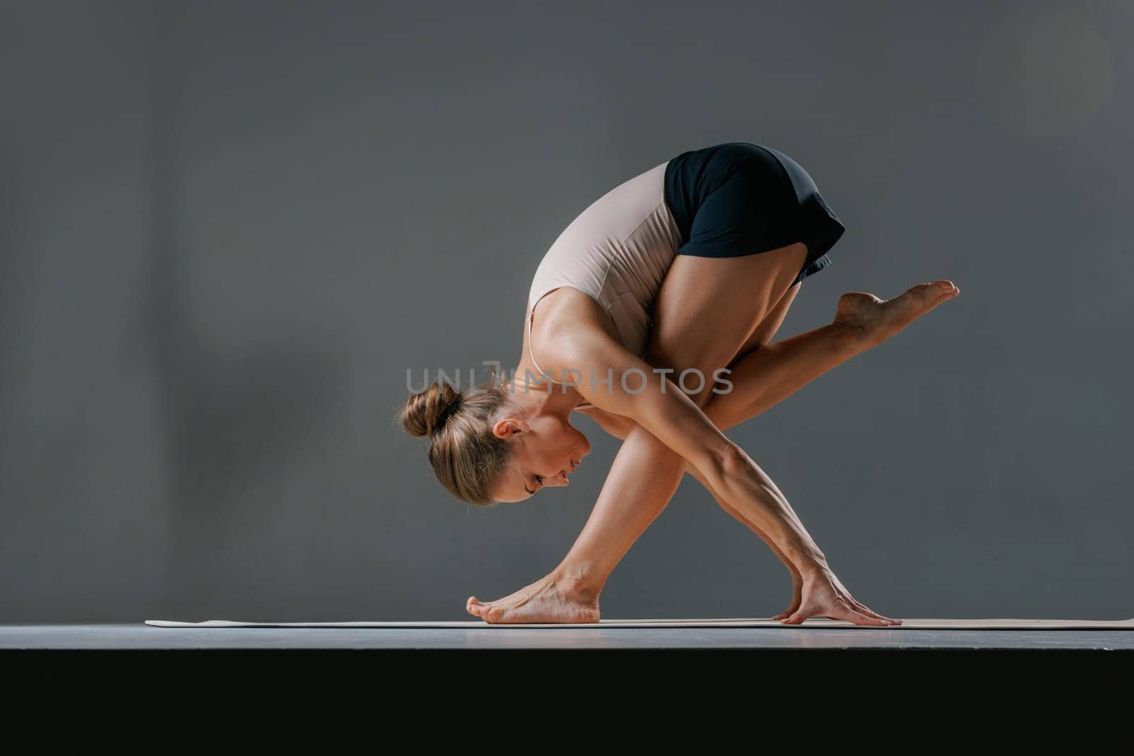 An athletic young woman performs the stretching pose Baddha Parsvakonasana, or Bound Side Angle Pose, during her daily yoga practice at a studio.