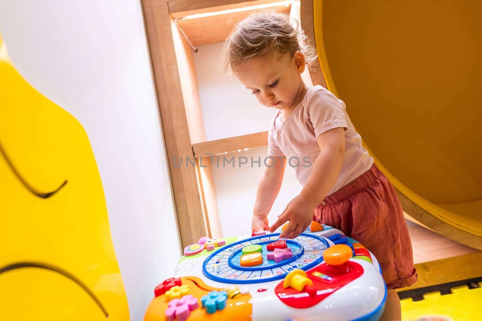 Toddler playing with colorful interactive activity table in a vibrant indoor playroom