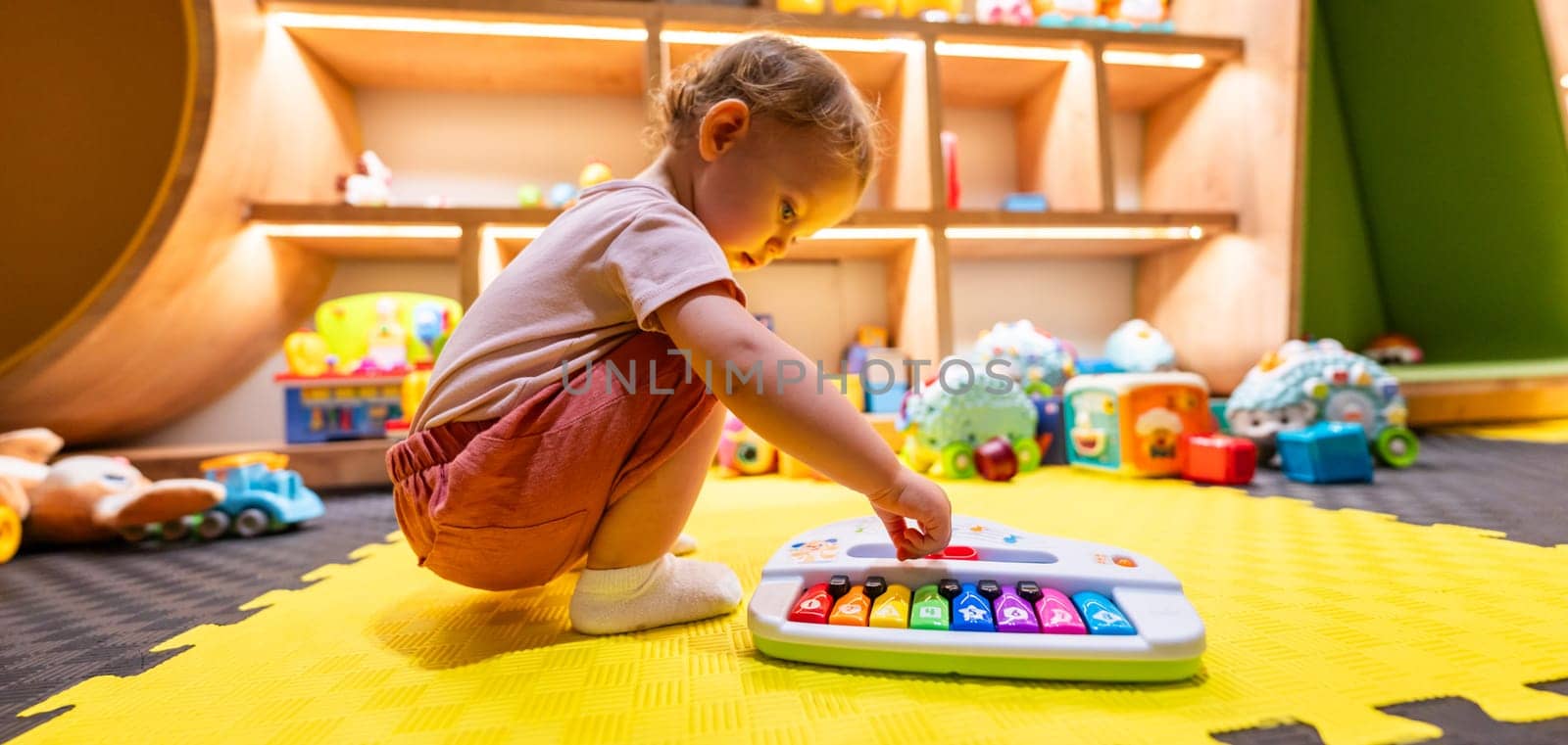 Toddler playing with a colorful toy piano in a bright indoor playroom