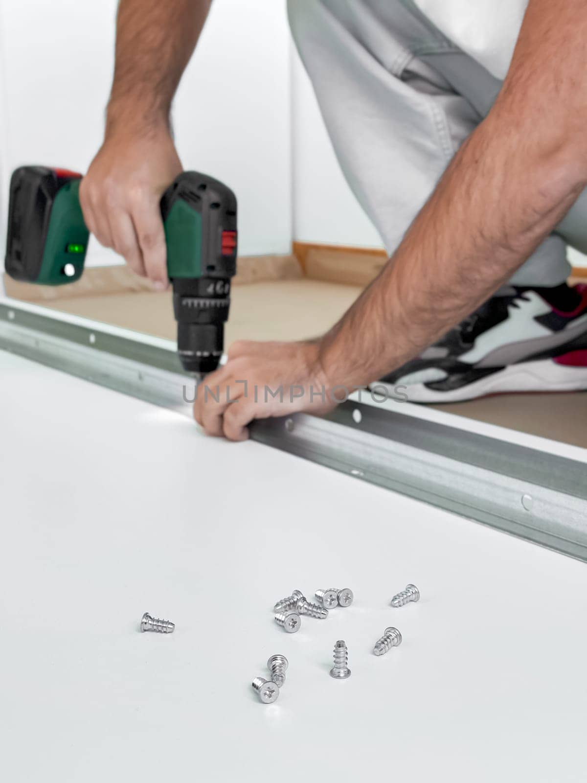 Caucasian male adult using drill to assemble metal frame with screws.