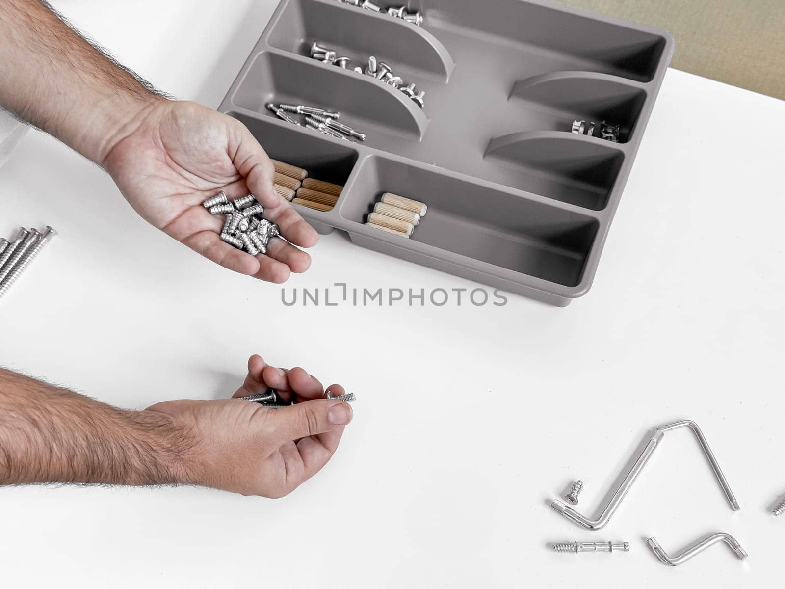 Assembling furniture. Hands organizing screws and dowels near tray.
