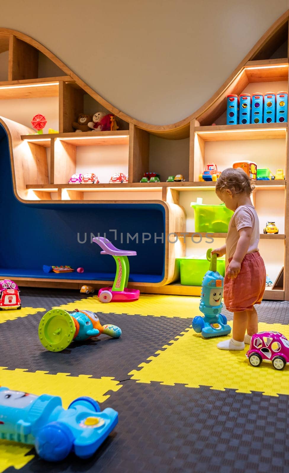 Young child enjoying a playful indoor activity space with toys, shelves, and creative designs