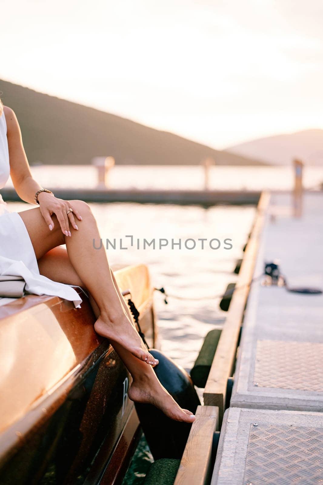 Barefoot woman sits on board a yacht moored at the pier. Cropped. Faceless. High quality photo