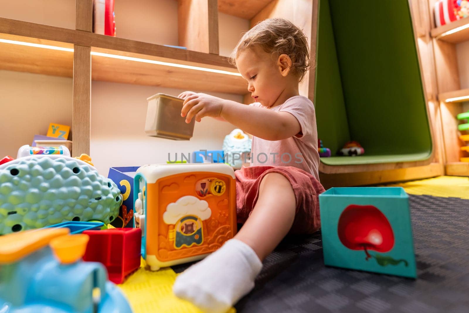 Toddler playing with educational blocks in colorful indoor playroom for kids