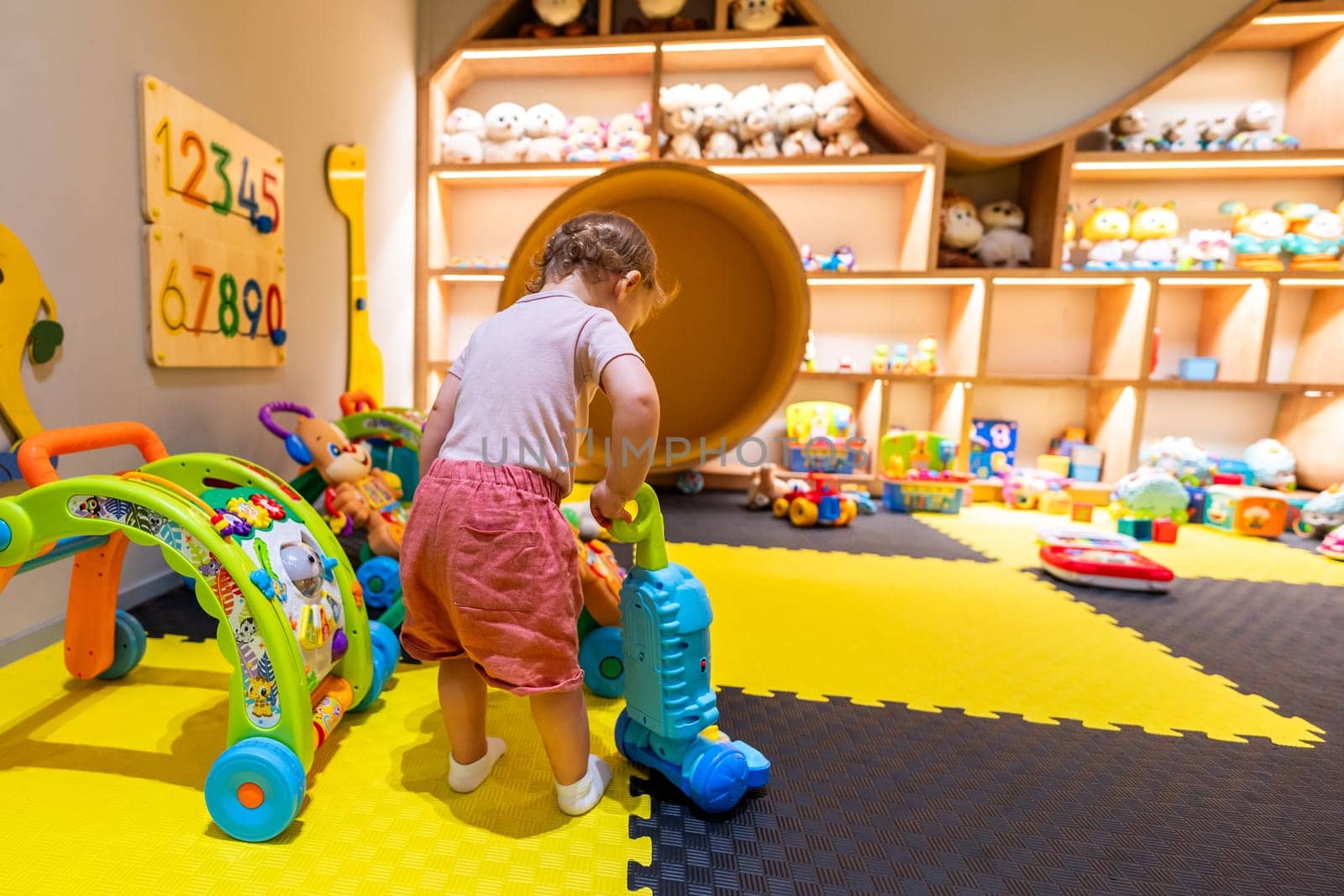Toddler playing with a toy vacuum cleaner in a colorful playroom filled with educational toys and activities