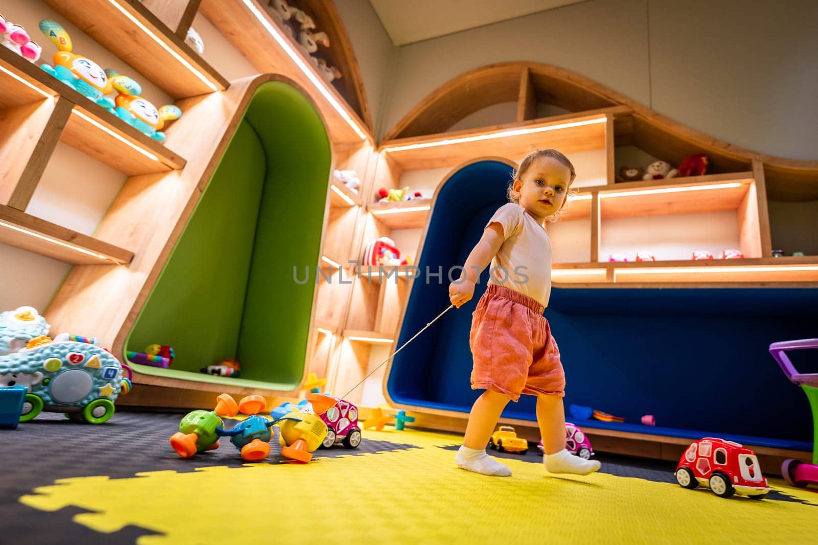 Active toddler exploring a colorful indoor playroom filled with toys, games, and activity areas for fun and learning