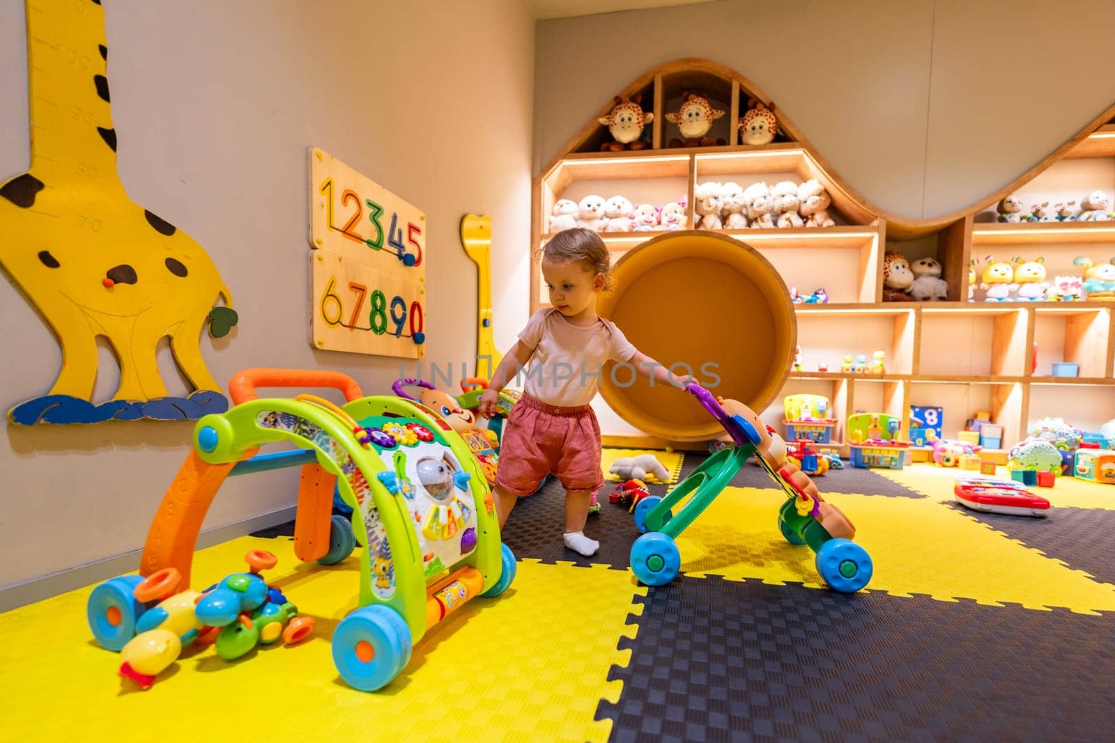 Toddler exploring an educational indoor playroom with colorful toys, activity walkers, and interactive learning tools for growth and fun