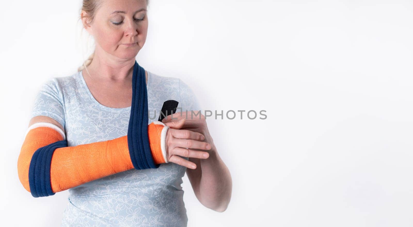 middle aged woman with broken arm in cast hangs her arm in a sling, modern treatment methods, on a neutral background, copy space,
