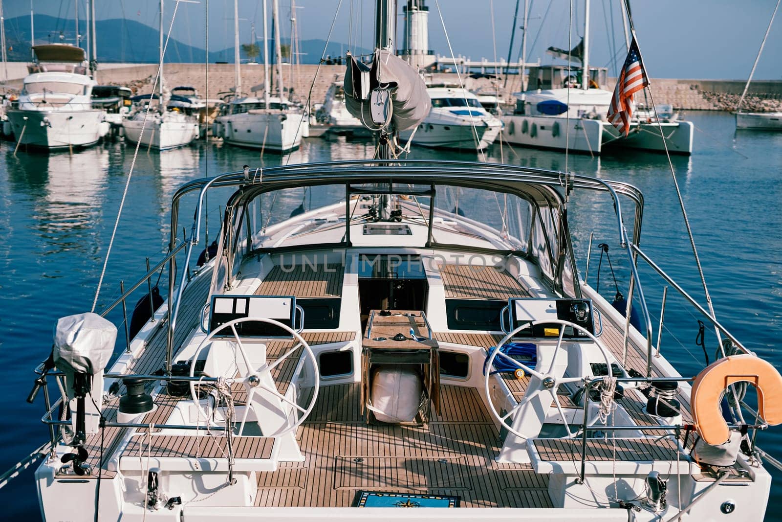 Sailing yacht with two steering wheels and wooden deck is moored at the pier. Back view. High quality photo