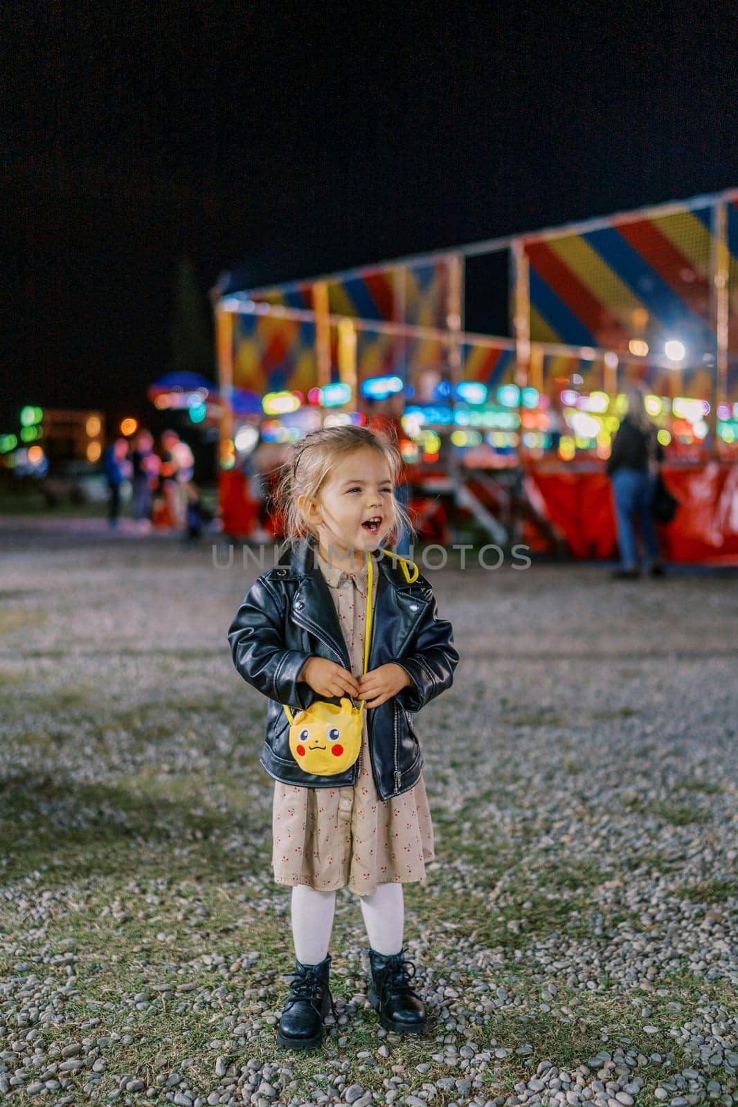 Little laughing girl stands near a colorful carousel. High quality photo