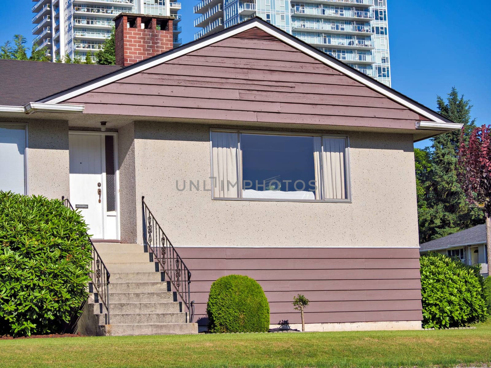 Green lawn and main entrance of average residential building on high rise and blue sky background in British Columbia, Canada.