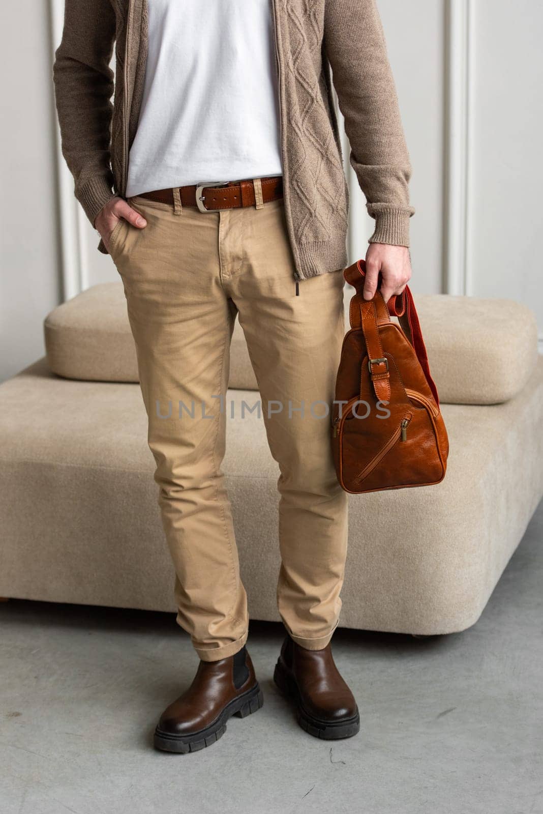 A fashionable man stands with a yellow brown hip bag in a contemporary room, embodying urban style and professionalism. Beige shirt and brown pants