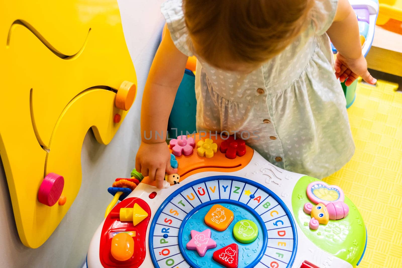 Toddler enthusiastically engaging with an educational toy in a vibrant playroom. Concept of joyful learning and promoting fine motor skill development in a fun environment