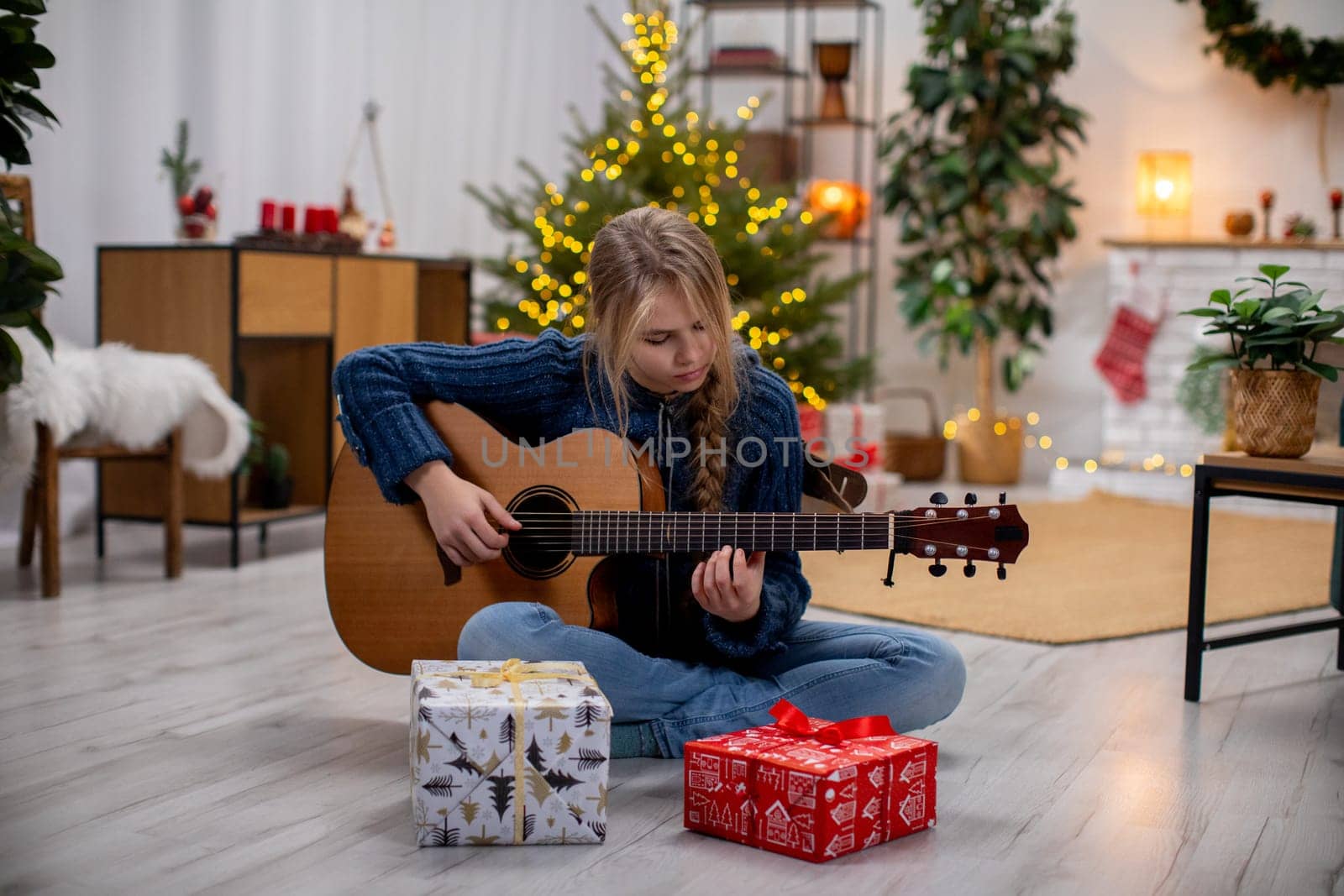 A young person happily playing guitar in a warm setting with Christmas decorations and wrapped gifts