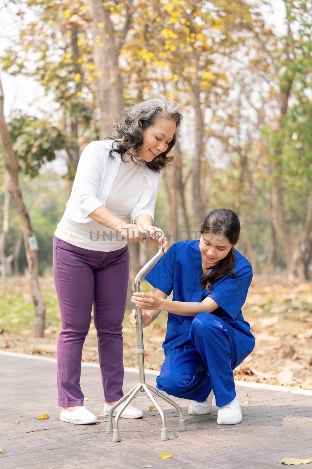 Nurse or female caregiver help senior woman holding stick to walk in the hospital garden.