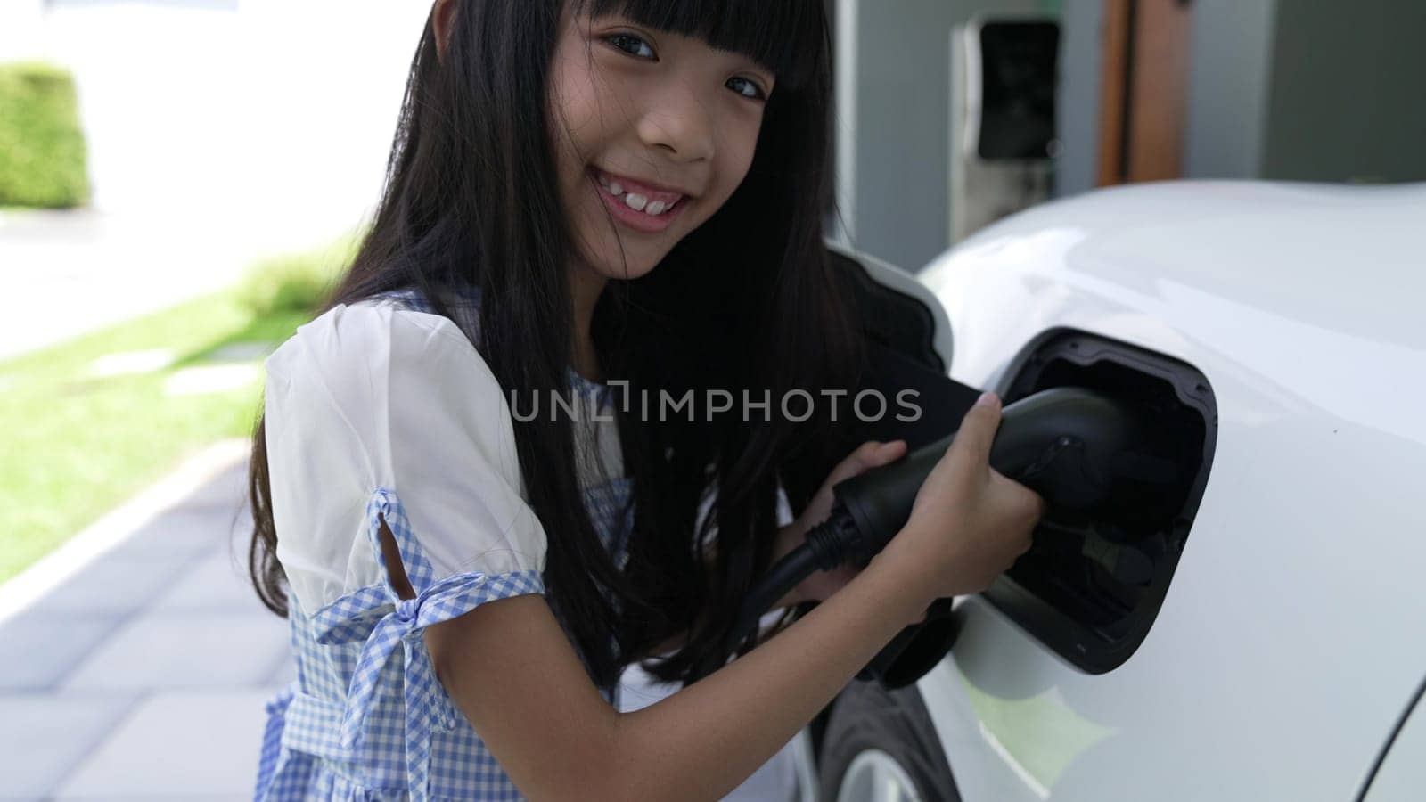 A playful girl holding an EV plug, a home charging station providing a sustainable power source for electric vehicles. Alternative energy for progressive lifestyle.