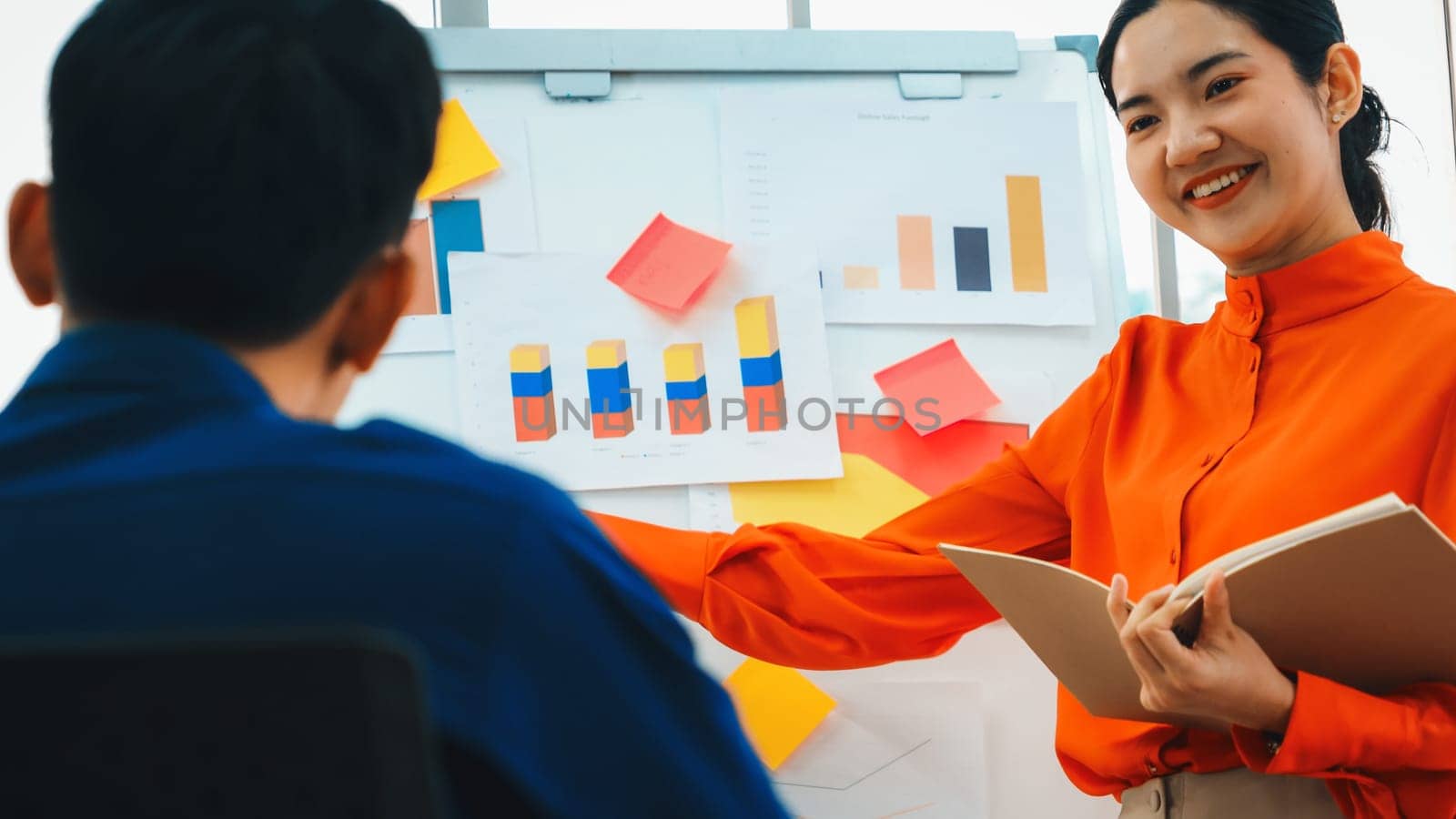 Young woman explains business data on white board in casual office room . The confident Asian businesswoman reports information progress of a business project to partner to determine strategy . Jivy