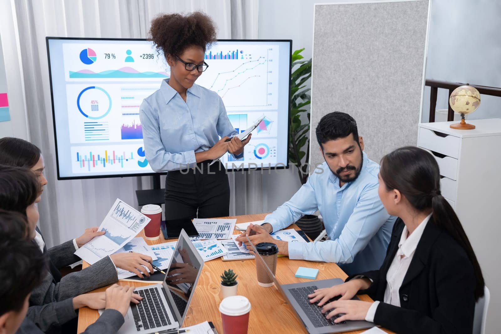 Young african businesswoman presenting data analysis dashboard on TV screen in modern meeting. Business presentation with group of business people in conference room. Concord