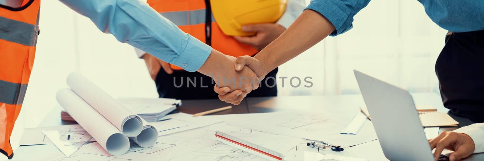 Construction engineer handshake with businessman contractor over architecture design blueprint on meeting table. Architect and engineer shake hand after successful cooperation teamwork. Insight