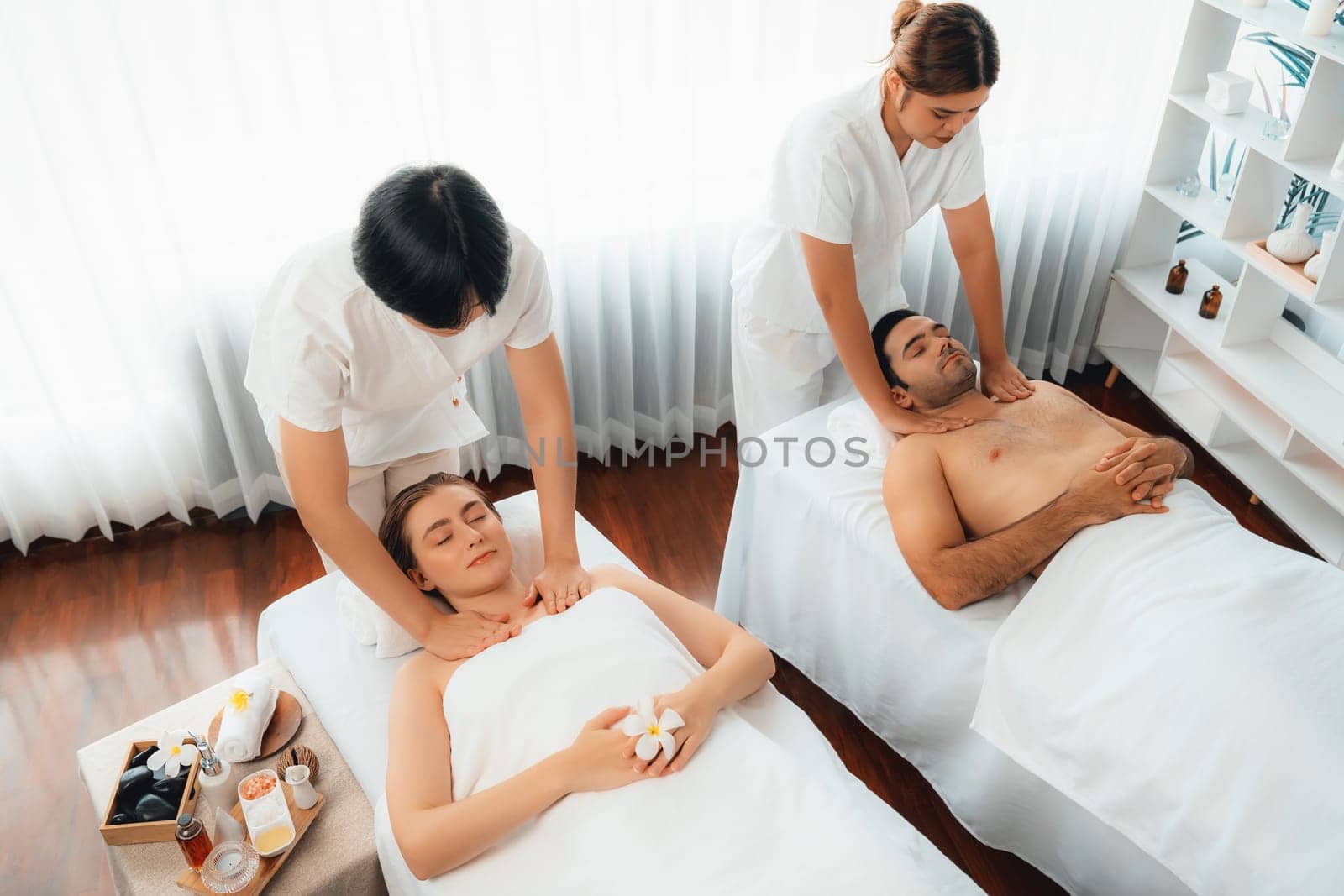 Caucasian couple customer enjoying relaxing anti-stress spa massage and pampering with beauty skin recreation leisure in day light ambient salon spa at luxury resort or hotel. Quiescent
