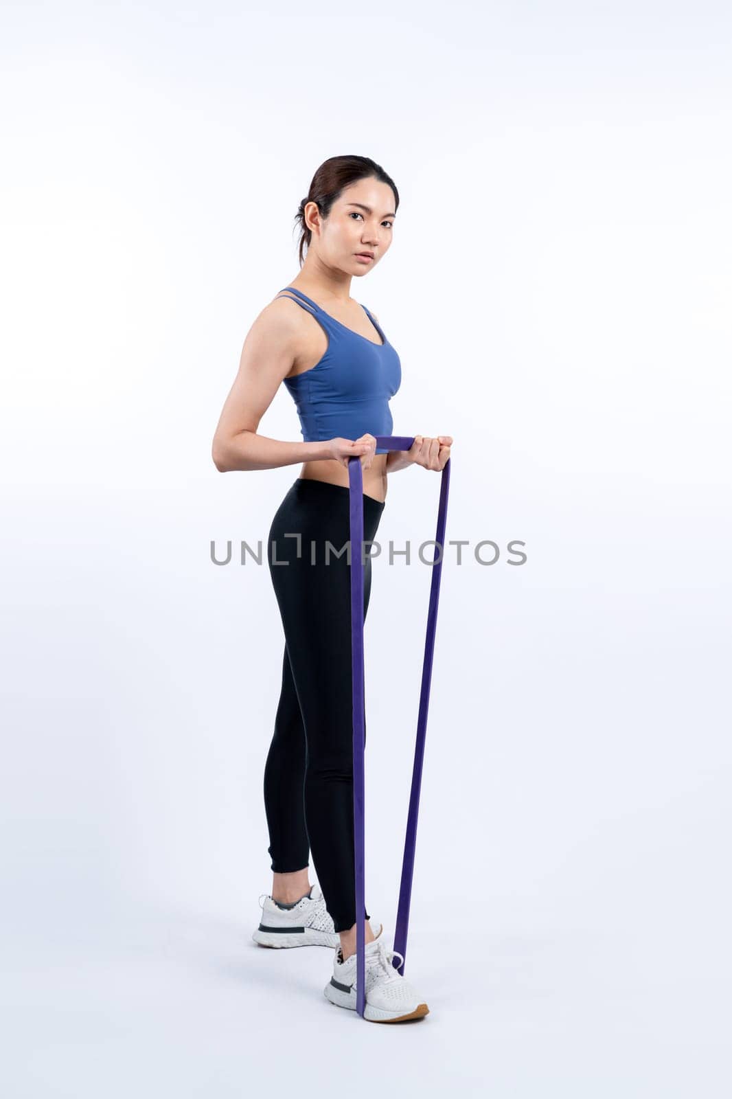 Vigorous energetic woman in sportswear portrait stretching resistance sport band. Young athletic asian woman strength and endurance training session workout routine concept on isolated background.