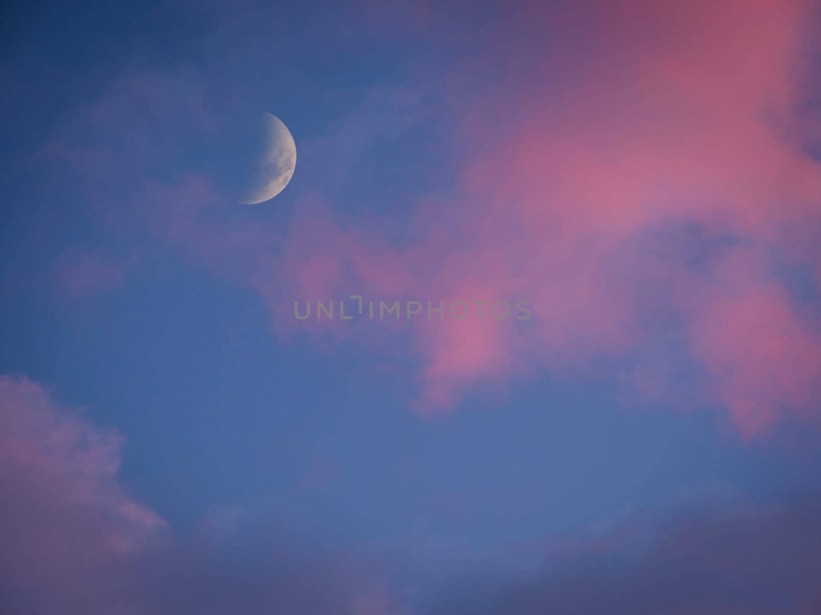 A half moon in the sky with a pink cloud