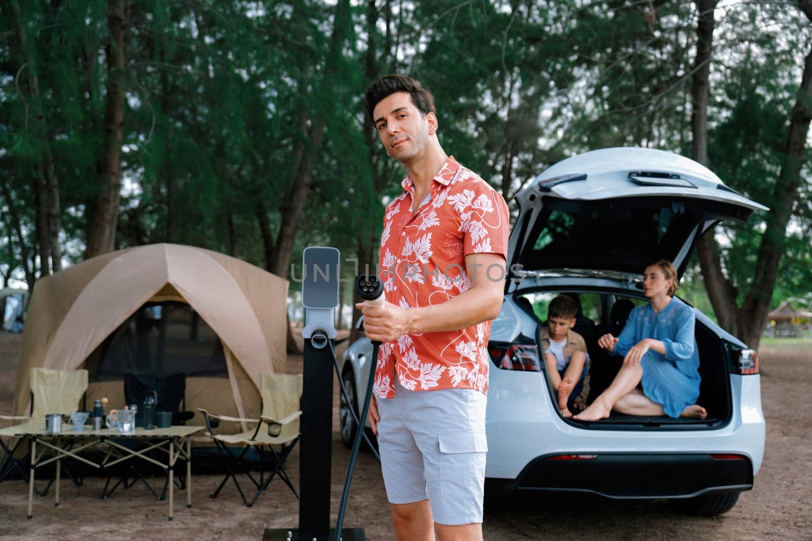 Outdoor adventure and family vacation camping in nature travel by eco friendly car for sustainable future. Lovely family recharge EV car with EV charging station in campsite. Perpetual