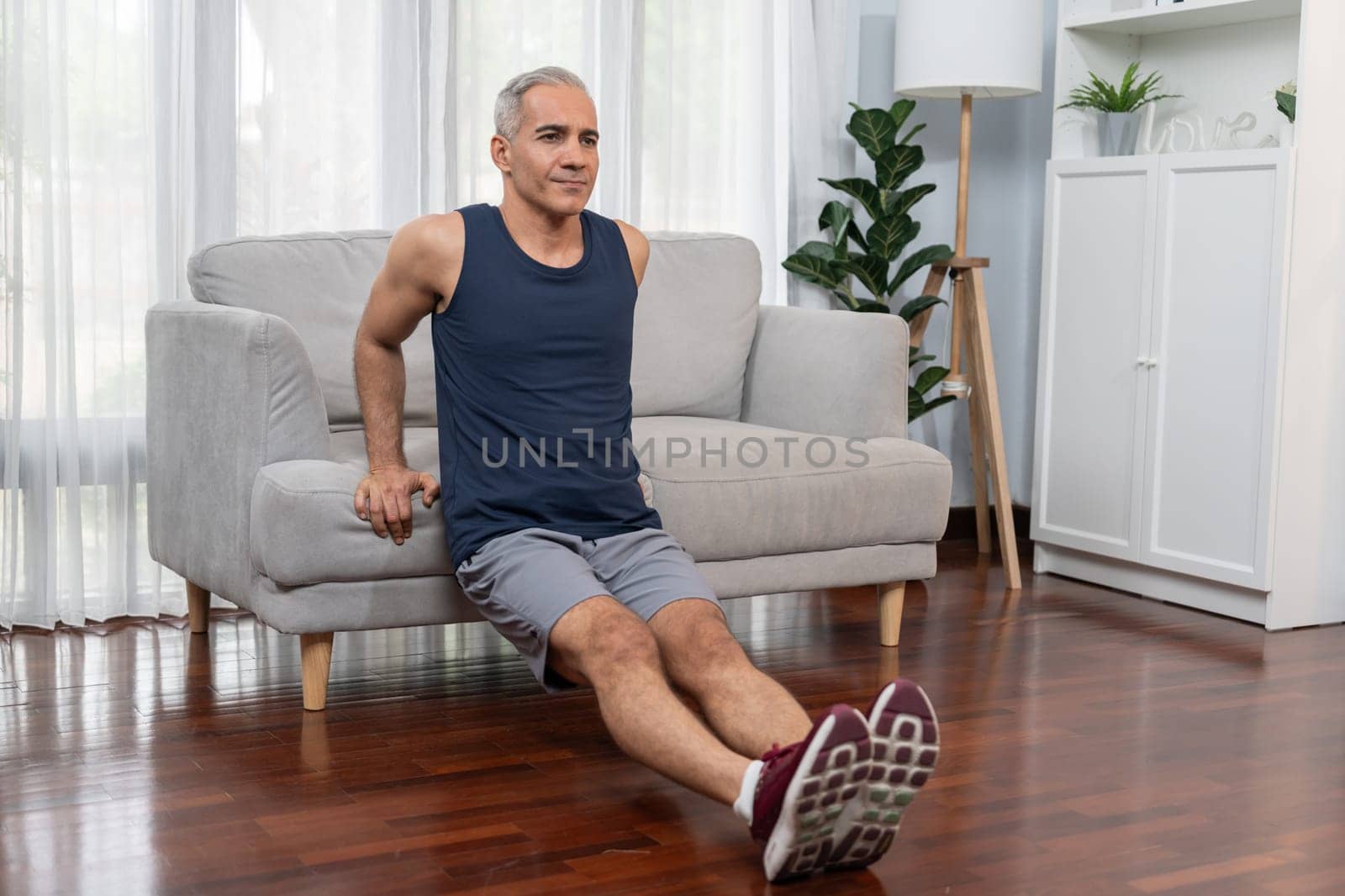 Athletic and active senior man using furniture for effective targeting muscle with push up at home exercise as concept of healthy fit body lifestyle after retirement. Clout