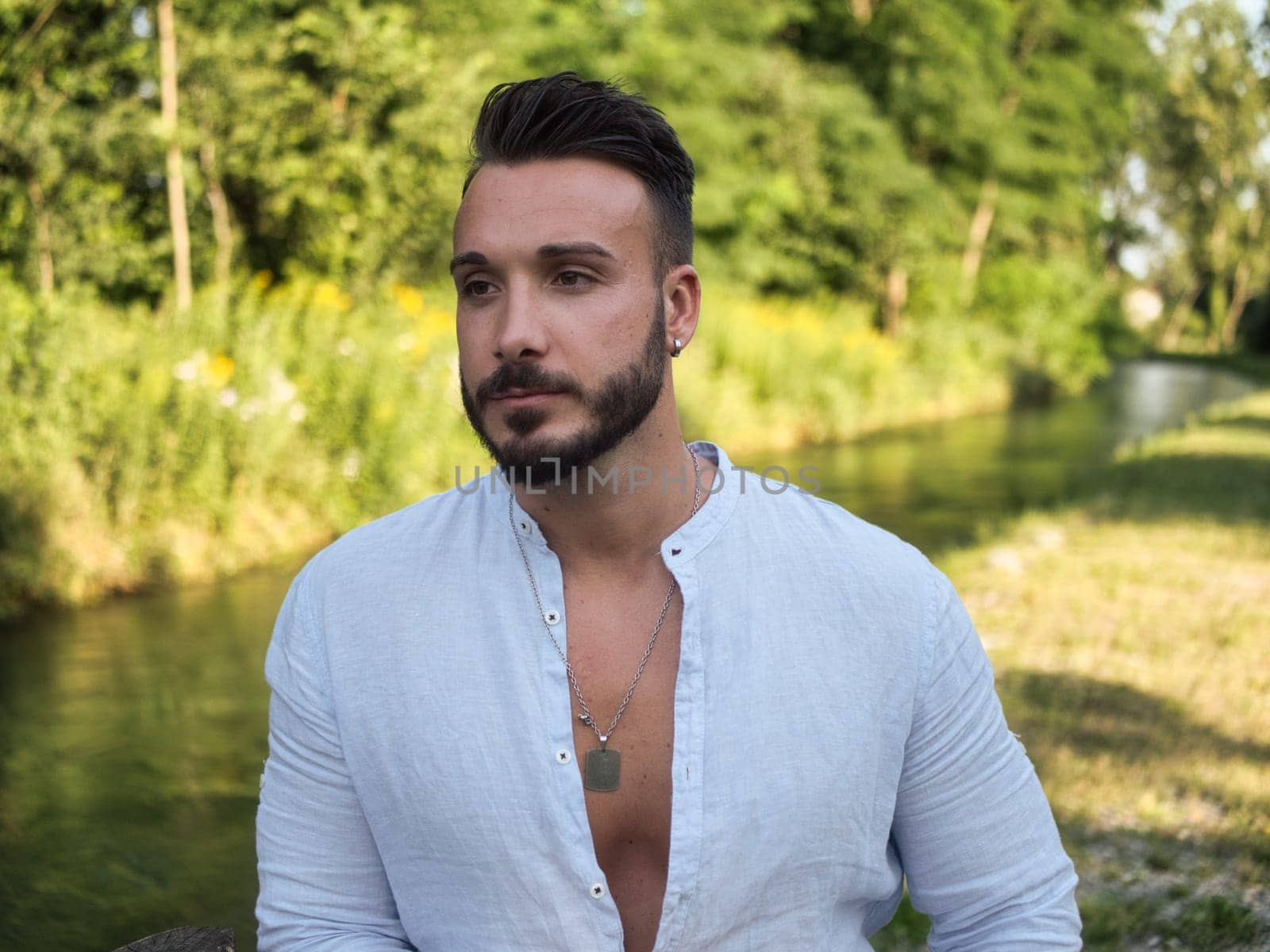 A man standing in front of a water stream. Photo of a man contemplating the serene beauty of a tranquil body of water