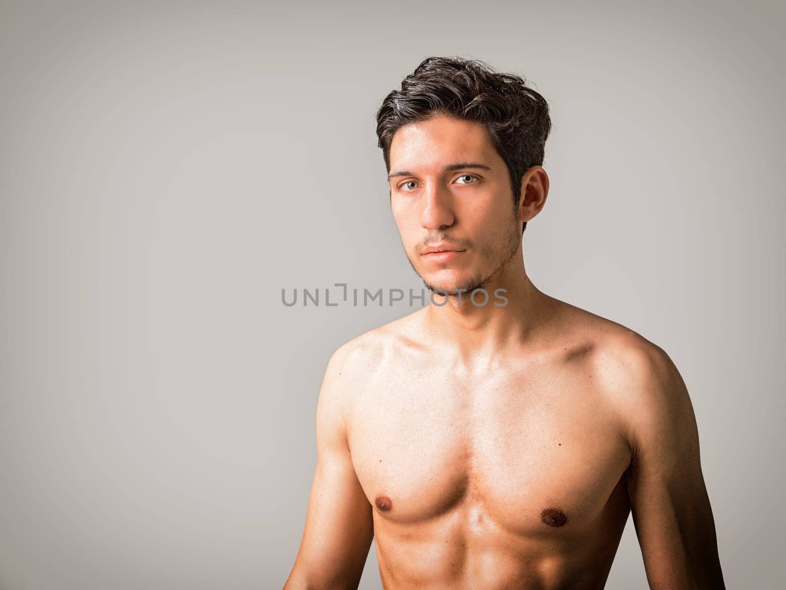 A man without a shirt posing for a picture in studio. Photo of a young and handsome shirtless man posing with captivating green eyes