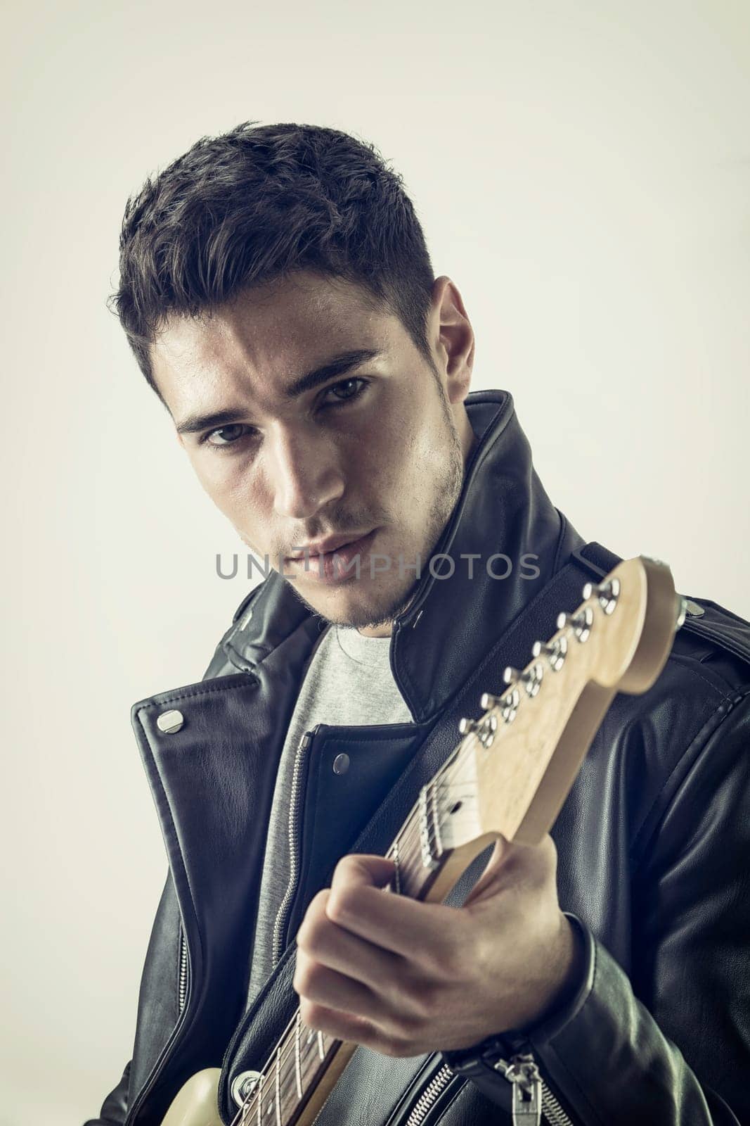 A man in a leather jacket holding a guitar. Photo of a musician rocking out in studio with his guitar
