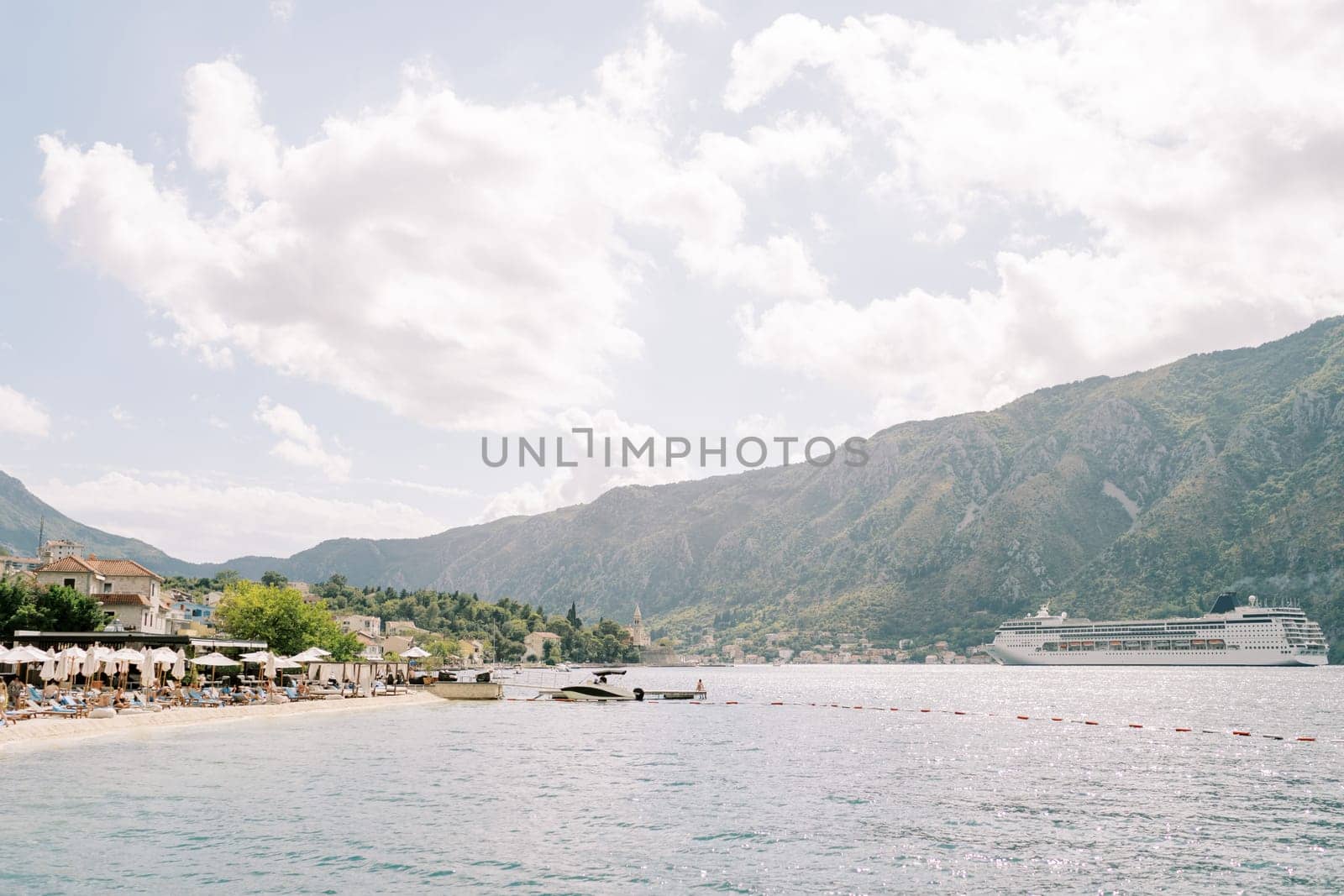 Huge cruise ship sails along the Bay of Kotor past the coast with mountains in the background. High quality photo