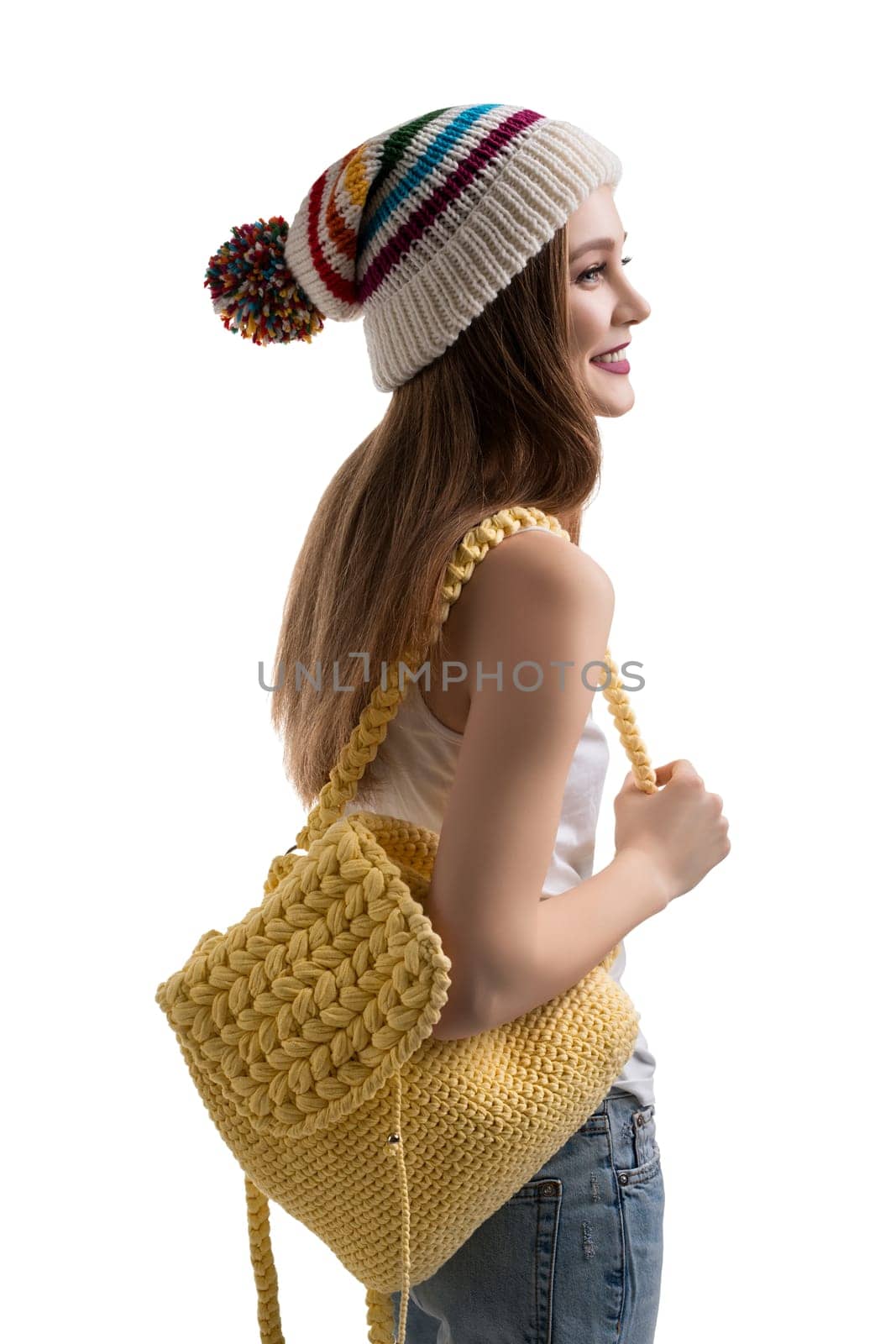 Side view of trendy young female with cute knitted backpack smiling and looking away while standing on white background