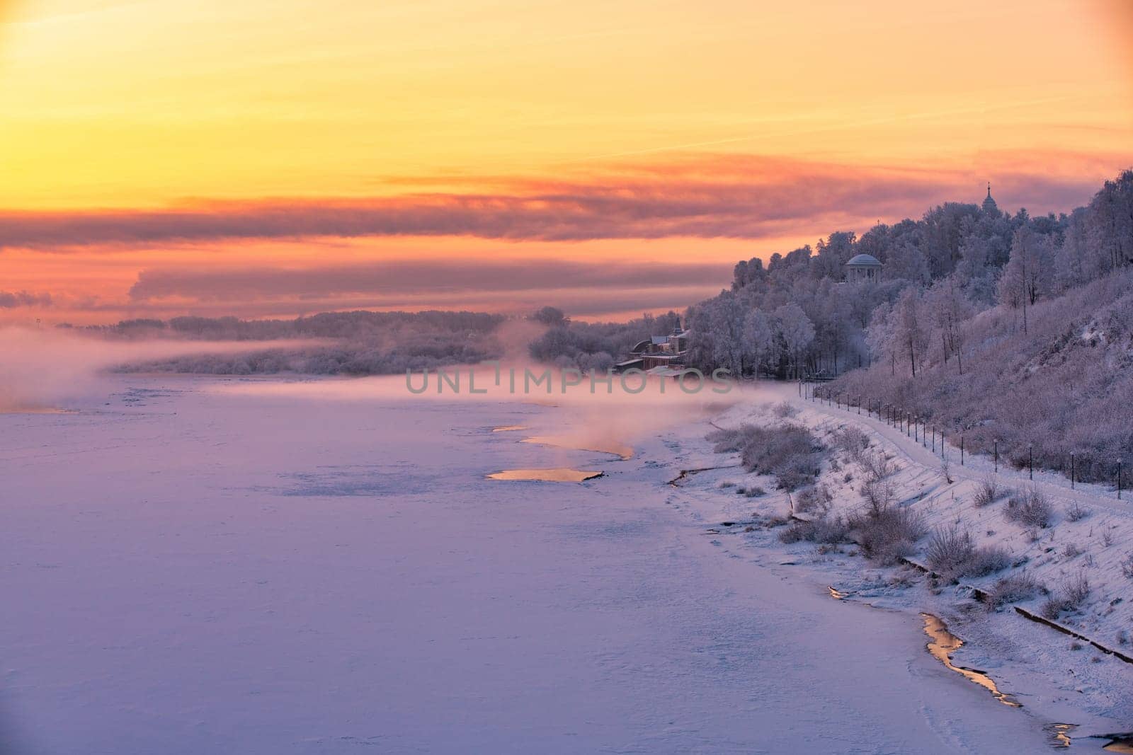 Beautiful Russian winter landscape with frozen river, embankment and street lamps against pink and yellow sunset view