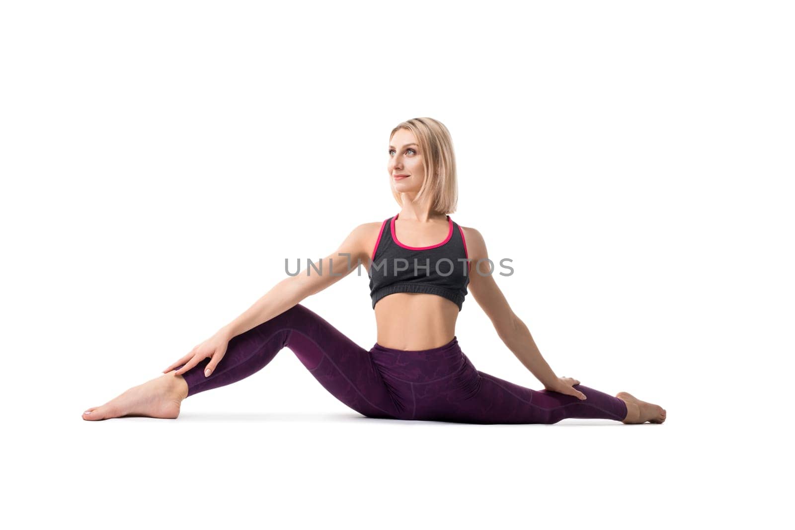 Slim blonde in sportswear sitting in a split on the floor doing yoga isolated view
