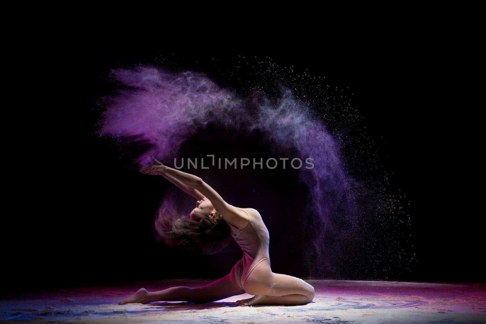 Gorgeous woman wearing beige body sitting in a split in color dust in dark room profile shot