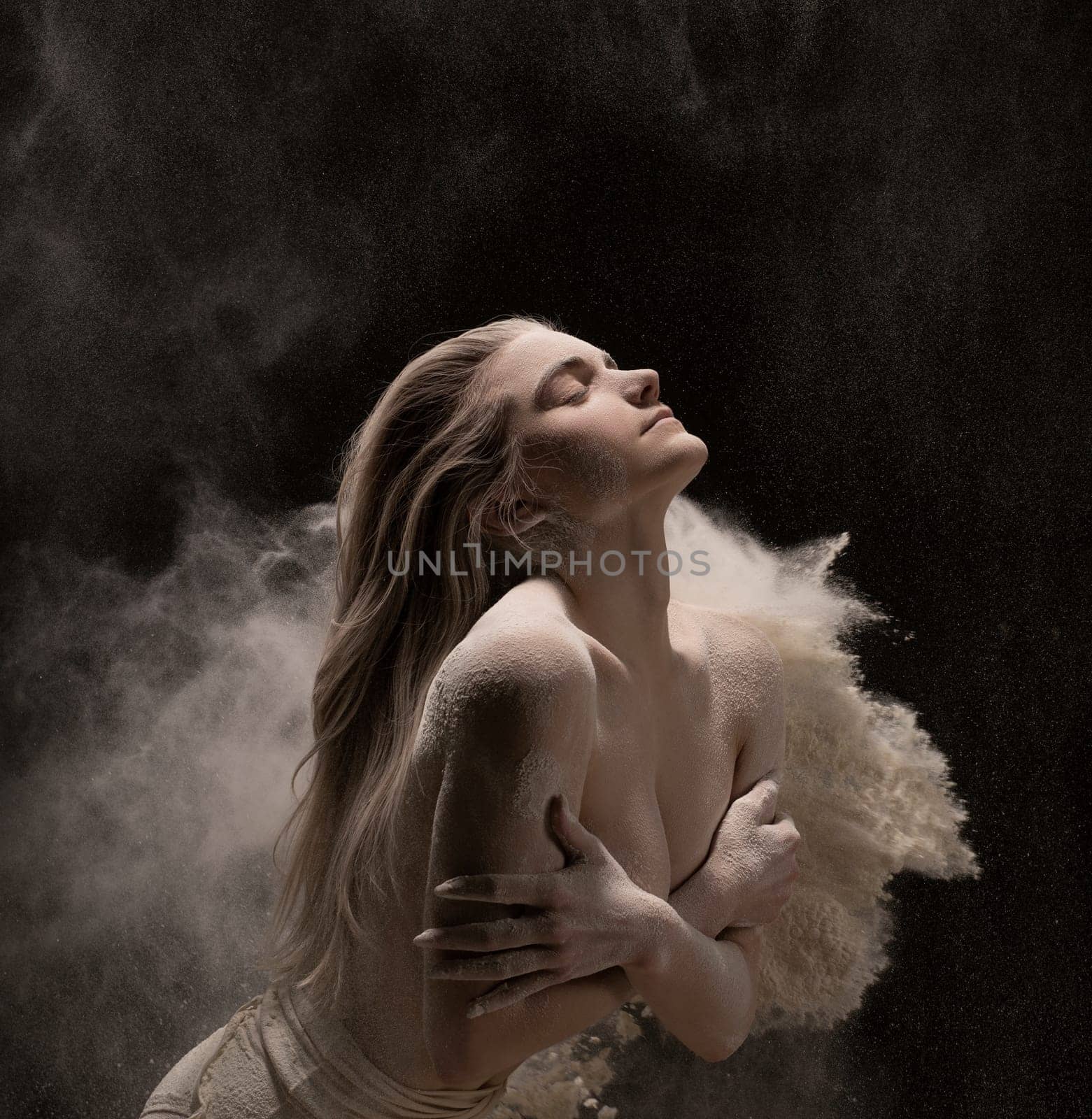 Young woman with long hair posing nude covering breast being all covered with white powder