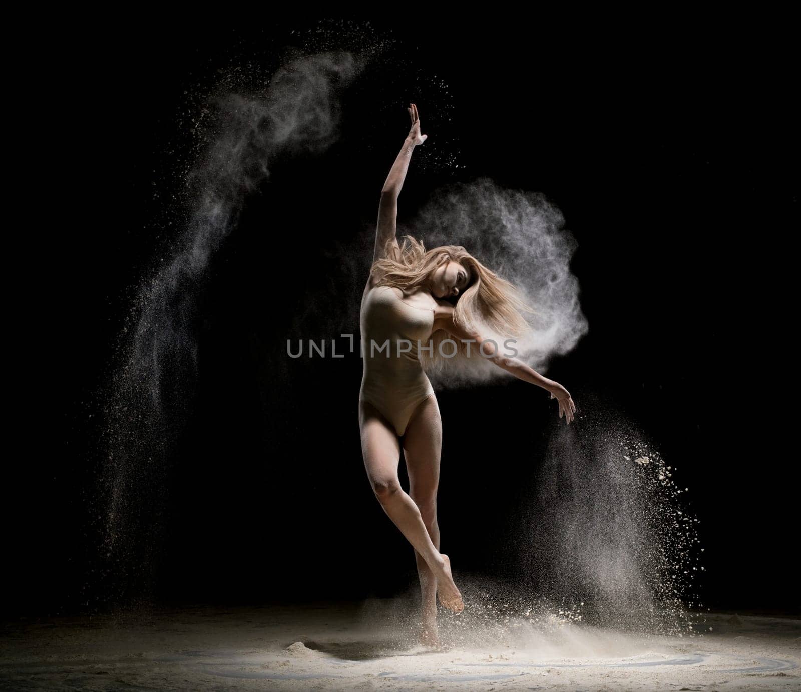 Gorgeous girl wearing beige body dancing in white dust in dark room