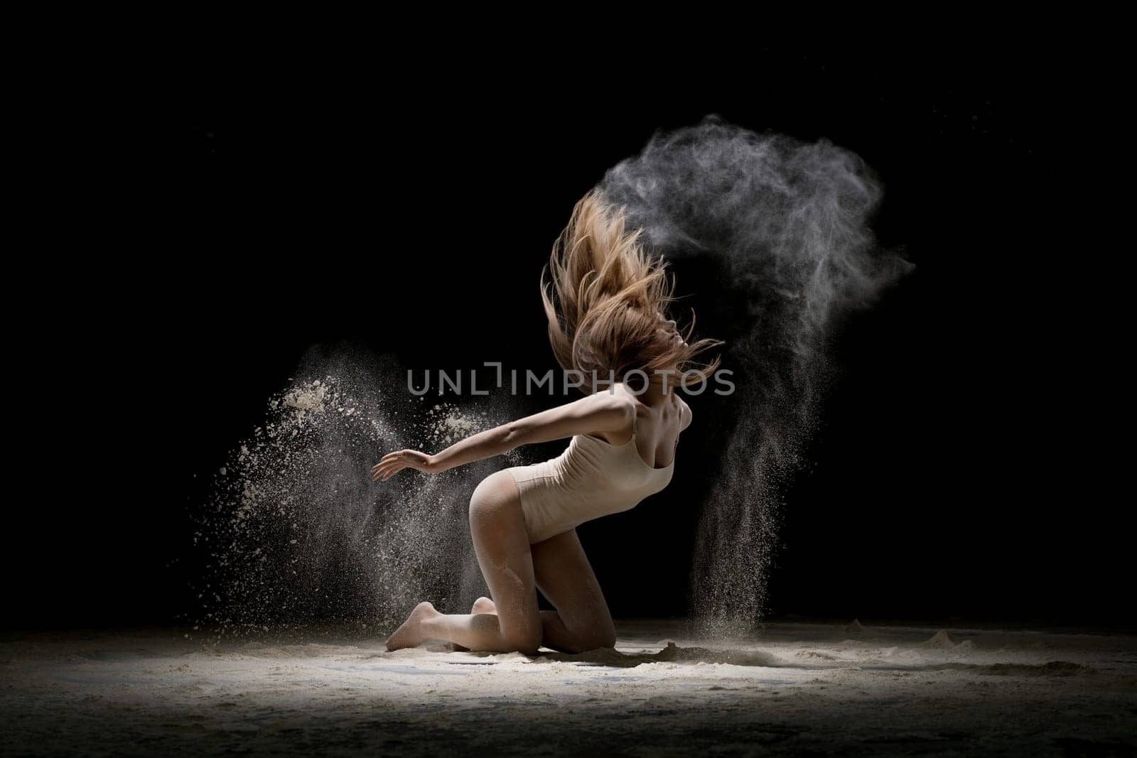 Gorgeous brunette wearing beige body staying on her knees in white dust in dark room shot