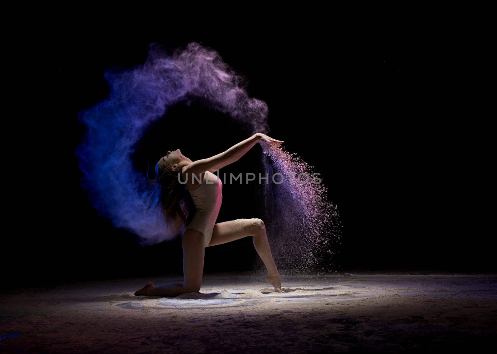 Gorgeous brunette wearing beige body staying on her knees in color dust in dark room profile shot