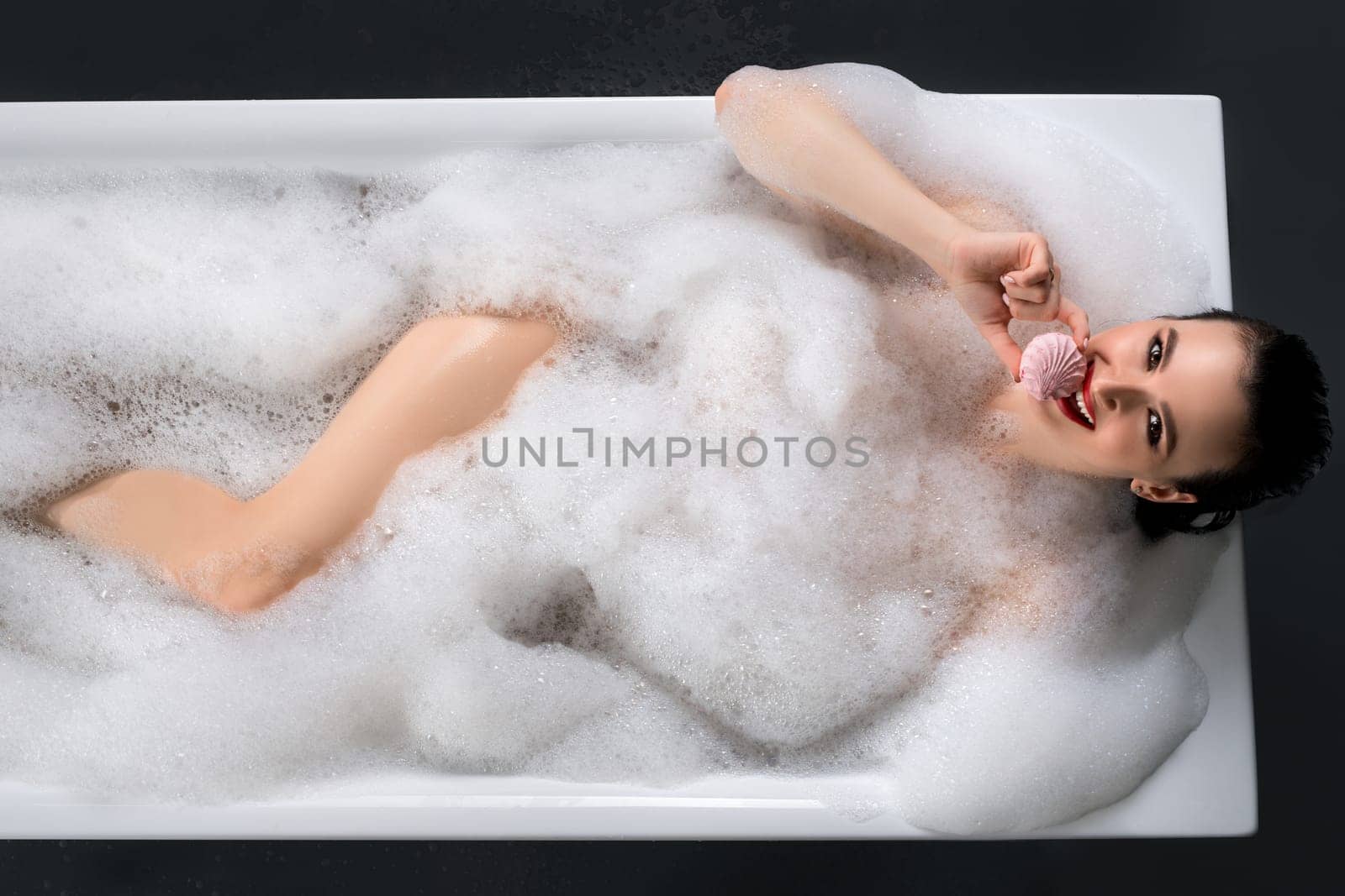 Gorgeous brunette in the nude bath having bath with foam high angle shot