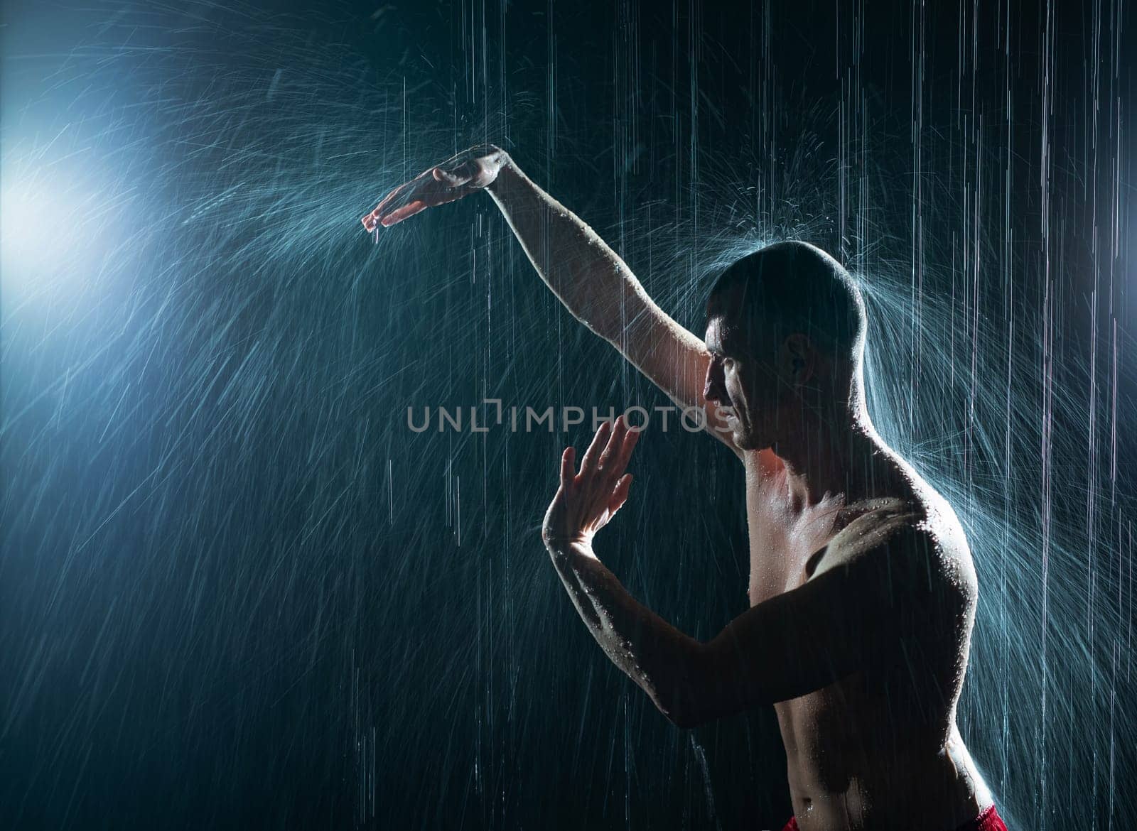Shirtless man practicing gymnastics under the rain in the dark profile cropped shot