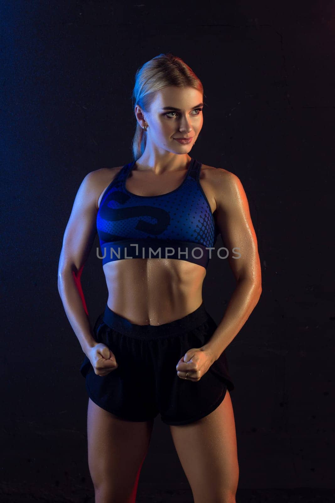 Athletic slim girl wearing top and shorts cropped view against dark wall