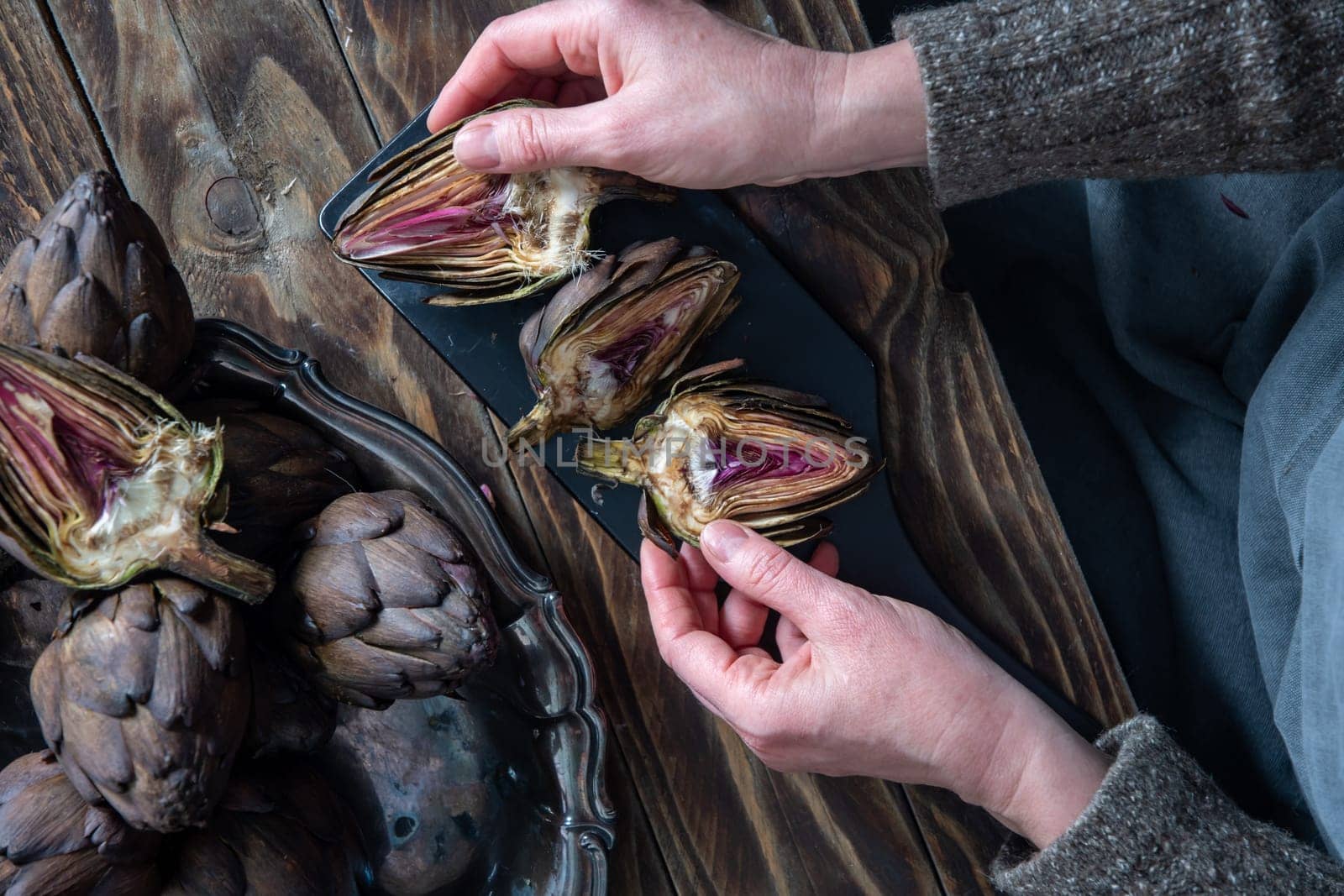 Woman cleaning fresh artichokes and cooking on wooden table, rustic still life top view,concept of healthy eating and fine dining,